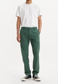 Gröna bomullshängselbyxor med rak passform, med knappstängning och sidofickor, i kombination med en enkel vit t-shirt och svarta sneakers.