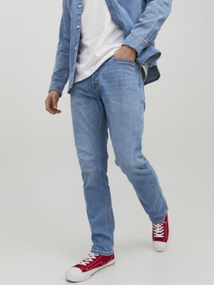Vaqueros de denim azul claro con corte recto, combinados con una camiseta blanca y zapatillas rojas con suelas y cordones blancos.