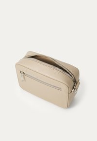 Sac pochette en cuir beige avec une surface texturée, doté d'une fermeture éclair sur le dessus et d'une poche zippée à l'avant, de forme rectangulaire compacte.