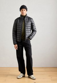 Sort quilted puffer jakke med høj krave, olivengrøn turtleneck, mørke jeans og grå sneakers med grønne striber.