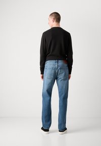 Blå jeans med en avslappet passform, i klassisk femlommers design og med et brunt lærmerke på baklivet. Kombinert med en svart genser.