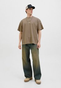 Hnědý oversize bavlněný tričko, světlé široké džíny, béžové gumové boty a šedá/černá čepice s logem. Jednoduchý řetízek.
