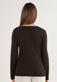 Brauner Pullover mit langen Ärmeln und strukturierter Oberfläche. Verfügt über einen dezenten Ausschnitt und eine taillierte Silhouette, die an der Hüfte endet.