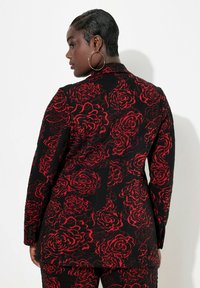 Černá bunda s červeným květinovým vzorem, texturovaná látka, dlouhé rukávy a knoflíky na manžetách, zobrazená zezadu na modelu.