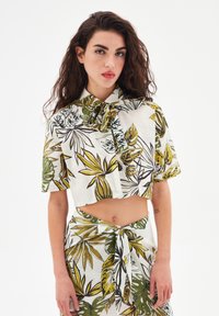 Camicia corta e gonna coordinata in tessuto leggero. Stampa tropicale di foglie verdi e gialle su sfondo bianco. Dettagli con legatura al colletto e in vita.
