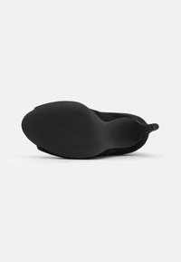 Suela de zapato de ante negro con un fondo de goma texturizado. Presenta un borde liso y una lengüeta trasera para facilitar su uso.