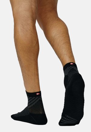 Schwarze Knöchelsocken mit strukturiertem Design, ausgestattet mit einem Mesh-Muster und einem roten und weißen Logo am Bündchen. Weicher Stoff, niedriger Schnitt.