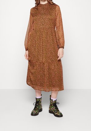 Braunes Midikleid mit Blumenmuster, langen transparenten Ärmeln, geknöpftem Kragen und gestuftem Rock. Kombiniert mit schwarzen Blumen-Combat-Stiefeln und pinken Socken.