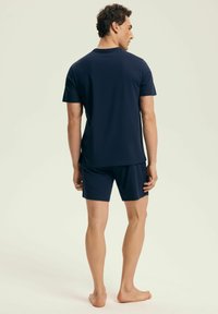 Granatowy zestaw koszuli z krótkim rękawem i szortów, wykonany z lekkiego materiału o gładkiej teksturze. Charakteryzuje się prostym wzornictwem i luźnym krojem.