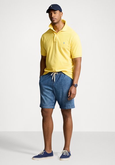 Polo shirt jaune avec un col montant, shorts en denim, casquette bleue marine et baskets bleues. Comprend un logo sur la chemise et des shorts ajustables.