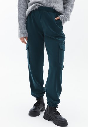 Teal joggers met een elastische tailleband en boorden, voorzien van zijzakken en een gladde textuur, gecombineerd met zwarte chunky laarzen.