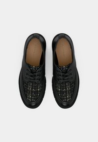 Chaussures noires à lacets avec un dessus texturé présentant un tissu à motifs. Semelle en caoutchouc avec bords arrondis et accents en cuir lisse.