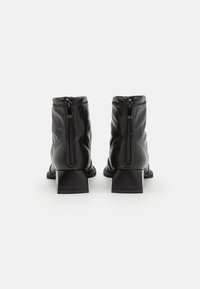 Bottes basses en cuir noir à finition lisse, avec une fermeture éclair à l'arrière et un talon carré texturé. Design simple, lignes épurées.