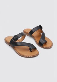 Sandalias de cuero negro con diseño de tira, correa ajustable en el tobillo, plantilla color marrón y costuras blancas en contraste a lo largo de la suela.