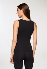 Top senza maniche nero con un design aderente, scollatura rotonda, superficie liscia e orlo dritto, abbinato a leggings neri simili.