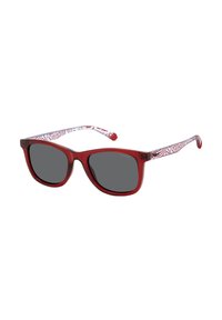 Lunettes de soleil en plastique rouge avec verres fonc�és, dotées d'une sangle blanche à motif. La monture a une forme carrée arrondie et une texture lisse.