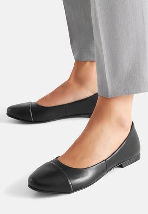 Černé baleríny z kůže s kulatou špičkou a švem přes přední část. Podpatek je nízký a stélka se zdá být polstrovaná.
