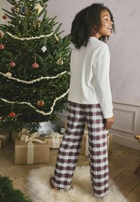 Vit tröja med långa ärmar ihop med rutiga byxor i rött, grönt och vitt med små hjärtmönster, mot en festlig bakgrund.