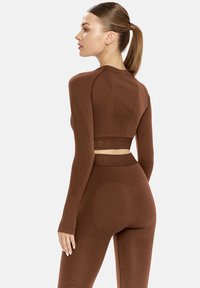 Barna bordázott hosszú ujjú crop top és illő leggings, amely szoros illeszkedésű, textúrált anyagból készült, logós pánttal és varrás nélküli tervezési részletekkel.