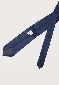 Cravate en soie pour homme bleu marine avec un motif texturé subtil, montrant l'étiquette intérieure et les détails de couture sur un fond blanc.