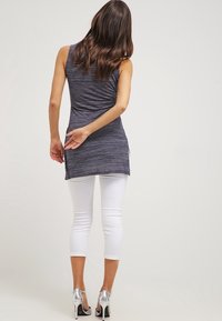 Top gris sin mangas con un ajuste relajado y una parte trasera más larga, combinado con leggings blancos cortos y zapatos de tacón alto plateados.