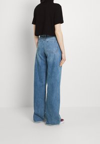 Svart kortärmad t-shirt matchad med ljusblå vida denimjeans, som har hög midja, två bakfickor och fransade fållar.