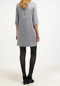 Grå, knälång klänning med trekvartsärmar, med bakknäppning och mjuk textur. Bärs med svarta strumpbyxor och klackskor.