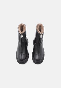 Bottes ankle en cuir noir avec une fermeture éclair à l'avant, doublées de doux fourrure marron. Semelle en caoutchouc noire épaisse, présentant des côtés texturés pour une meilleure adhérence.