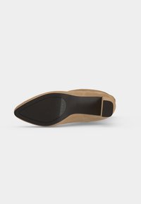 Semelle d'une chaussure beige à bout pointu avec des parties adhérentes en caoutchouc noir au talon et à l'avant de la semelle sur un fond clair uni.
