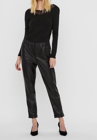 Black long-sleeve top with lace neckline and black faux leather tapered pants, featuring an elastic waistband and smooth texture.