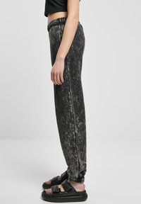 Svarte velour joggebukser med slim fit, elastisk midje og mansjetter ved anklene, med en marmor-lignende tekstur og sidesømmer.