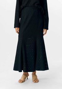 Sort, lang A-linje nederdel lavet af tekstureret stof med en diamantmønster og udskæringer. Båret med beige, open-toe hæle.