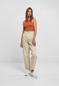 Lys beige vide benbukser kombinert med en tettsittende rustfarget tanktopp og hvite joggesko; bukser har høy midje og avkortet hem. 