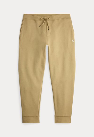 Beige joggerbroek met trekkoord in de taille, zijzakken en een klein wit geborduurd logo op de rechterdij.