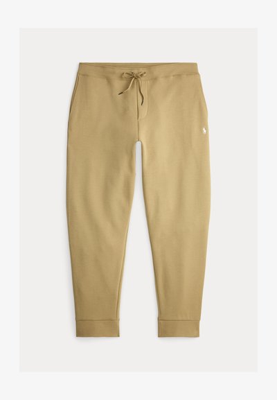 Beige joggerbroek met trekkoord in de taille, zijzakken en een klein wit geborduurd logo op de rechterdij.