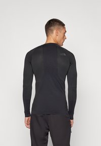 Schwarzes Langarm-Sportoberteil mit strukturierten Einsätzen, tailliertem Design und einem dezenten Logo auf dem oberen Rücken, aus atmungsaktivem Material.