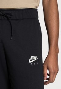 Svarta Nike sweatpants med dragsko i midjan, slät yta och vit "Nike Air"-logga på vänster lår.
