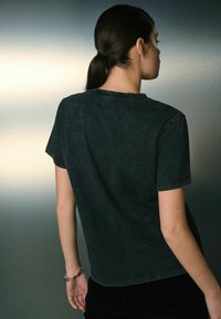 Czarna, krótka koszulka z prostym okrągłym dekoltem, charakteryzująca się wyblakłą fakturą i wzmocnionymi szwami.