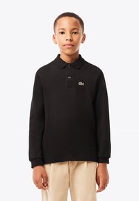Schwarzes Polohemd mit langen Ärmeln und drei Knöpfen, mit grünem Lacoste-Logo auf der Brust. Aus strukturiertem Stoff gefertigt.