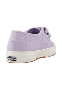 Sneaker en toile lavande claire avec une semelle en caoutchouc blanche, un design à lacets et un dos texturé, arborant un tab de marque sur le talon.