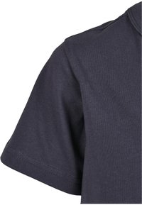 Gros plan sur un tissu en coton bleu foncé à manches courtes avec des coutures visibles sur la manche et la couture d’épaule.