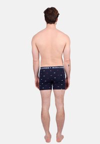 Boxer shorts bleu marine avec un motif composé de petits motifs animaliers rouges et blancs. Taille élastique avec la marque "MISE AUGREEN".