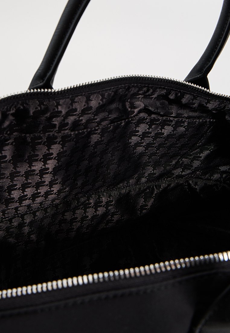 Bolso de mano negro con cremallera y forro interior que presenta un sutil patrón de espiga. Textura suave y asas redondeadas y resistentes.