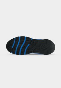Semelle en caoutchouc noire et bleue d’une chaussure de sport avec un motif de bande de roulement et des rainures segmentées pour l’adhérence et la flexibilité.
