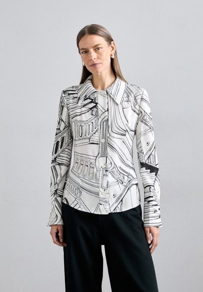 Bluză albă cu modele liniare negre, guler ascuțit și închidere cu nasturi. Mâneci lungi cu o formă ușor ajustată. Asortată cu pantaloni închisi la culoare.