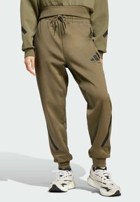Olivové športové tepláky s elastickým pásom, šnúrkou na stiahnutie, bočnými vreckami a čiernymi akcentmi pozdĺž nohavíc.
