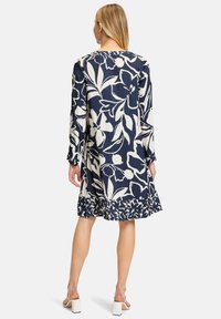 Marineblaues Kleid mit großem weißen Blumenmuster, langen Ärmeln und gerafftem Saum. Aus leichtem Stoff gefertigt, der florale Akzentdetails präsentiert.