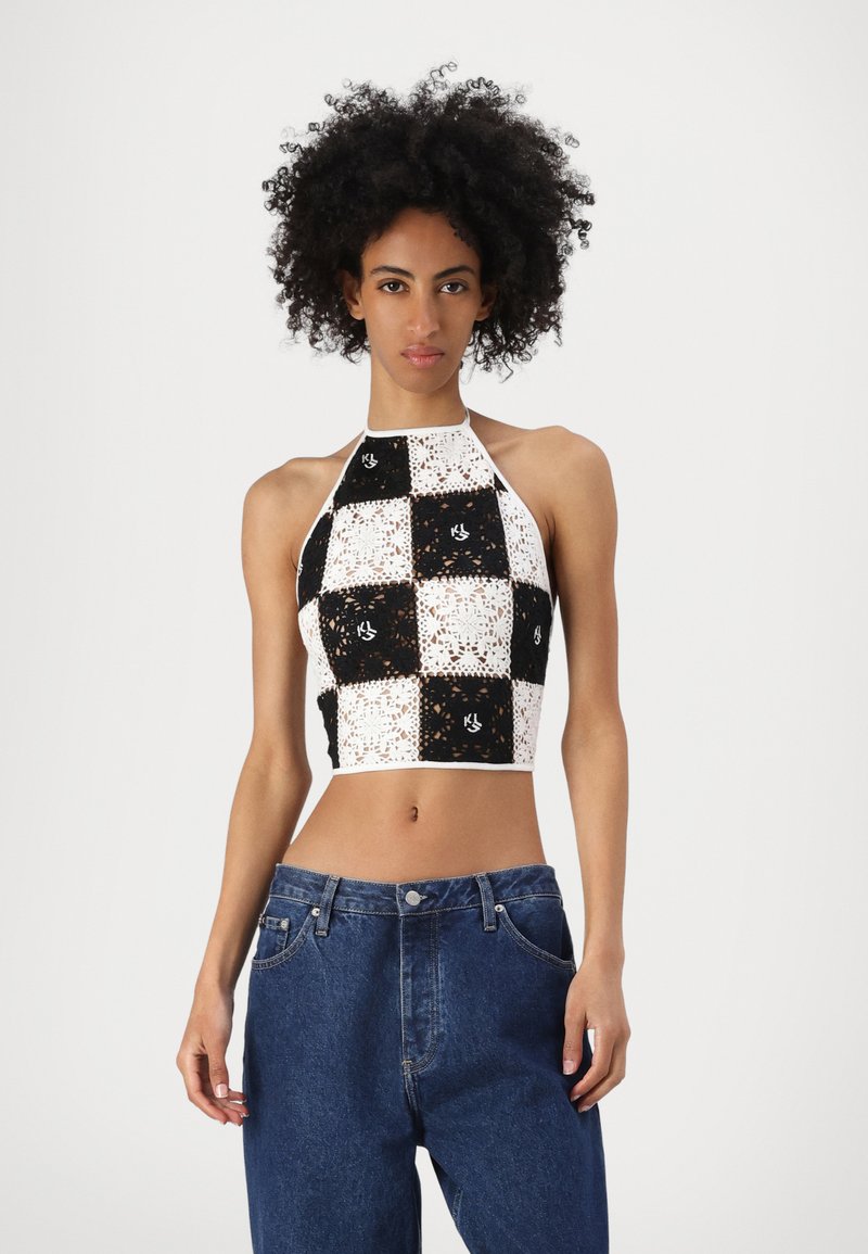 Top corto all'uncinetto con scollo a halter, caratterizzato da un design a scacchi bianco e nero, intricate fantasie e una silhouette aderente. Abbinato a jeans in denim blu.