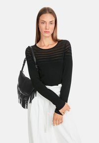 Schwarzes Langarmoberteil mit einem transparenten gestreiften Design am Ausschnitt. Kombiniert mit weißen Hosen und einer schwarzen Fransen-Handtasche.