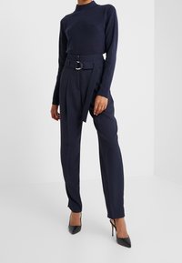 Granatowy sweter z prążkowanym wzorem i długim rękawem, zestawiony z granatowymi spodniami o podwyższonym stanie z dużą klamrą, uzupełniony czarnymi butami na wysokim obcasie.